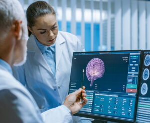 Two Medical Scientists in the Brain Research Laboratory Discussing Progress on the Neurophysiology Project Fighting Tumors. Neuroscientists Use Personal Computer with MRI, CT Scans Show Brain Images.