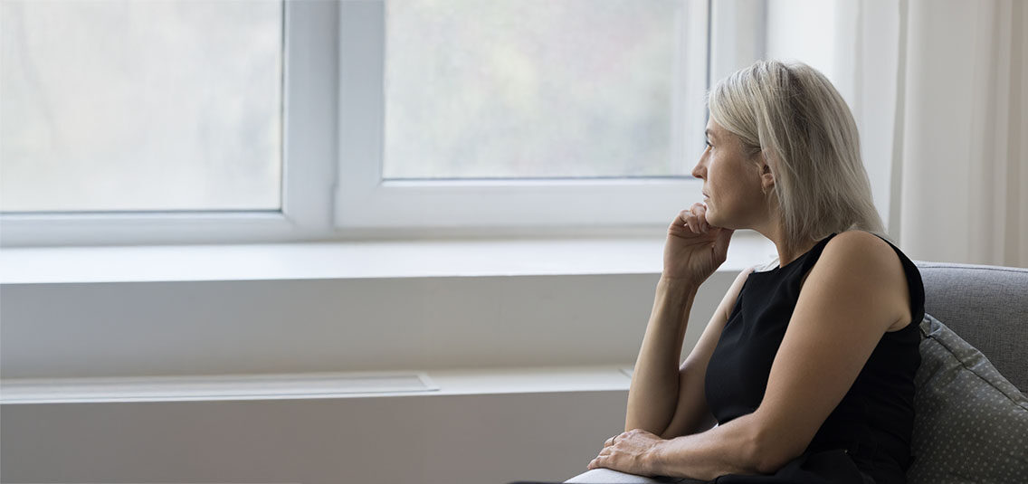 Mature woman sitting near a window in natural light, representing consideration of non-medication treatment options for depression, anxiety, and OCD